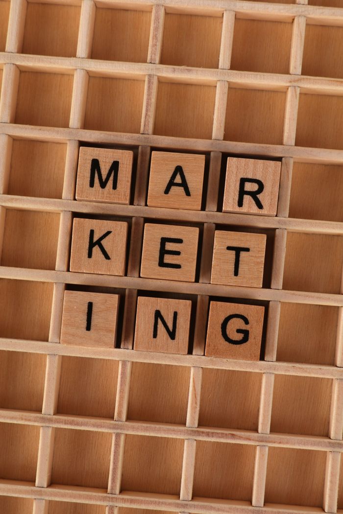 creative-01 Wooden letter tiles laid out to form marketing on a wooden grid, illustrating business strategy.